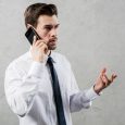 young-businessman-talking-smart-phone-gesturing-standing-against-grey-wall_23-2148087331